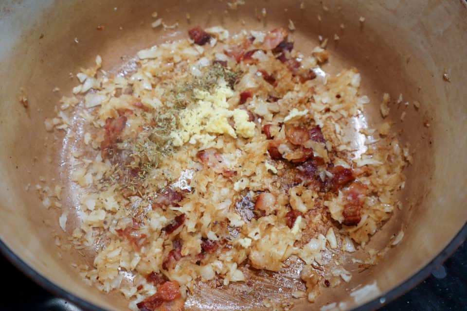 Close up of fried bacon, onionsm garlic and thyme at the bottom of a dutch oven as the base for New England Clam Chowder.