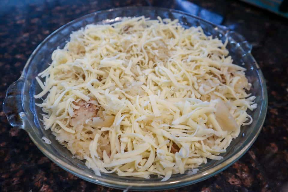 Picture of brats, sauerkraut and shredded cheese layered in a glass pie plate for Oktoberfest Pie.