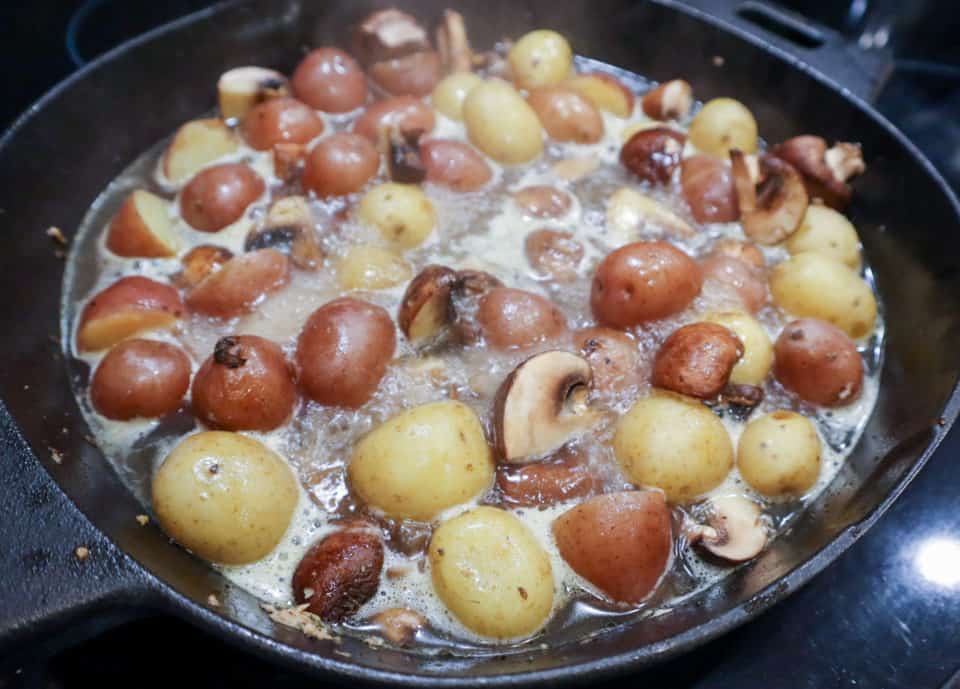Cast iron skillet filled with mushrooms, potatoes and bubbling broth.