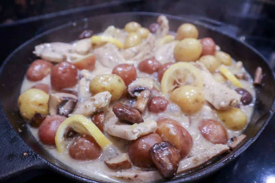 Cast iron skillet filled with bubbling pan sauce, chicken strips, potatoes, mushrooms and lemon slices.