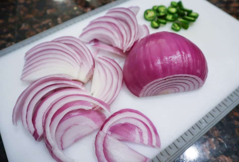 Red onions and sliced jalapenos on a cutting board.
