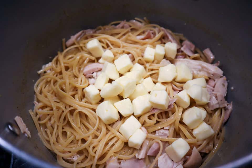 Adding chopped brie and chicken into the noodles in the stockpot.