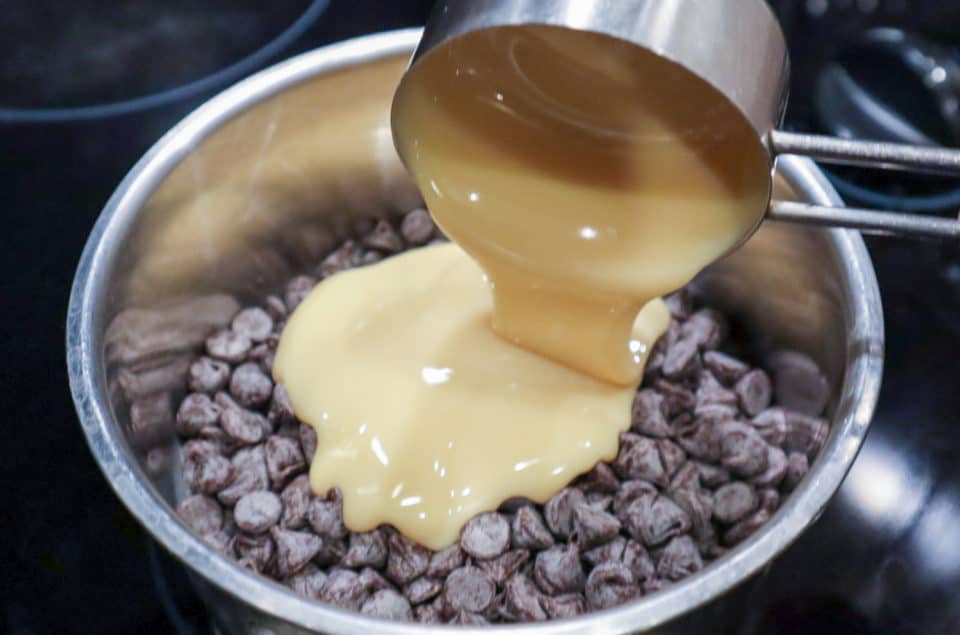 Sweetened condensed milk being poured over chocolate chips in saucepan.