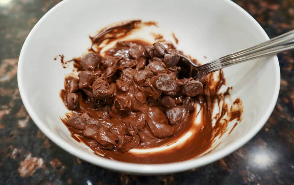 Semi melted chocolate chips in a small bowl with a spoon.