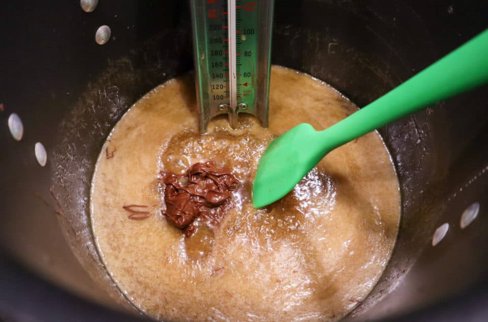 Ingredients for Chewy Chocolate Peanut Toffee in a pot with chocolate chips being mixed in.  Also green spatula and candy thermometer.