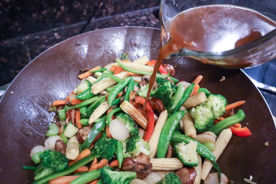 Stir fry sauce being added into the veggies and chicken in the skillet.