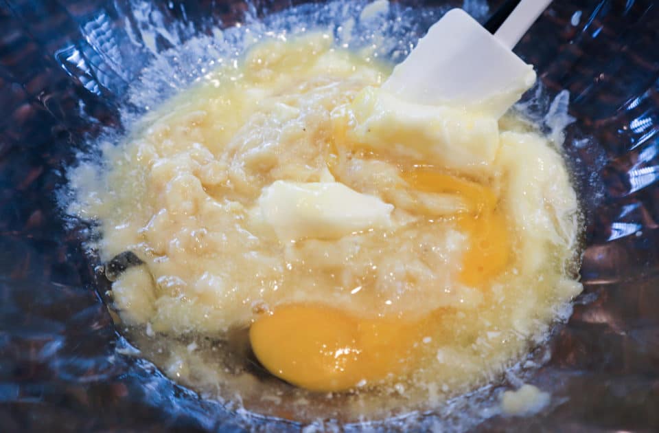 Oil, butter, egg and vanilla being mixed into banana in a bowl with a spatula.