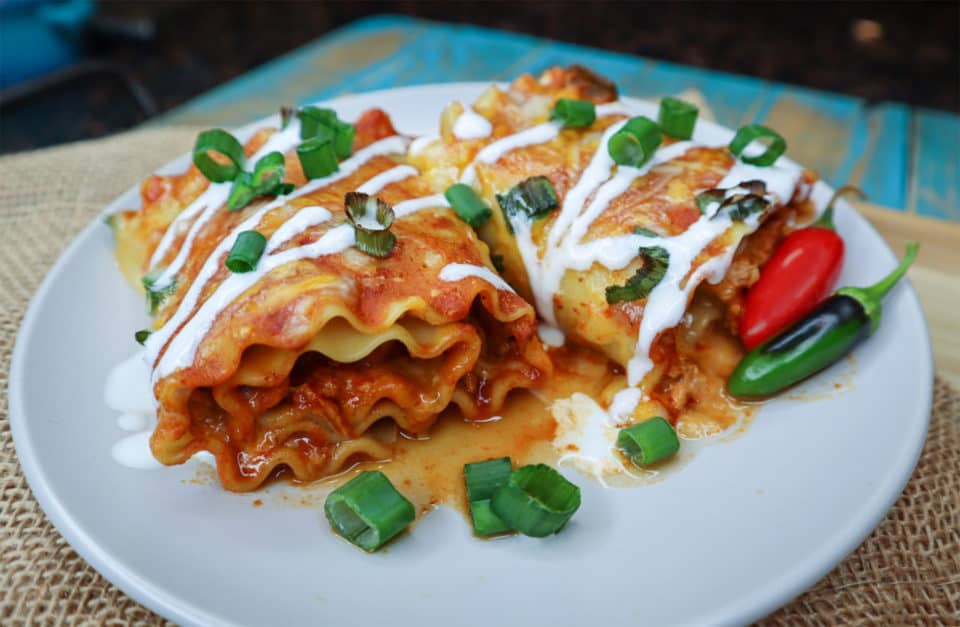 Finished picture of Baked Enchilada Lasagna Roll Ups on a plate, drizzled with sour cream.
