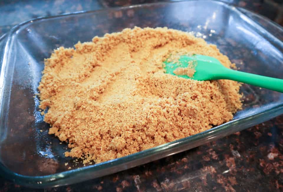 Packing the graham cracker crumb mixture down in the baking siah with a spatula.