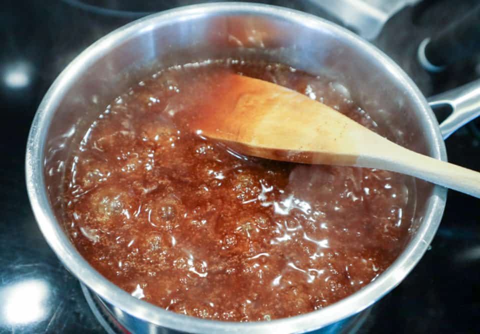 Sauce bubbling and visibly thickened in the saucepan with a wooden spoon.