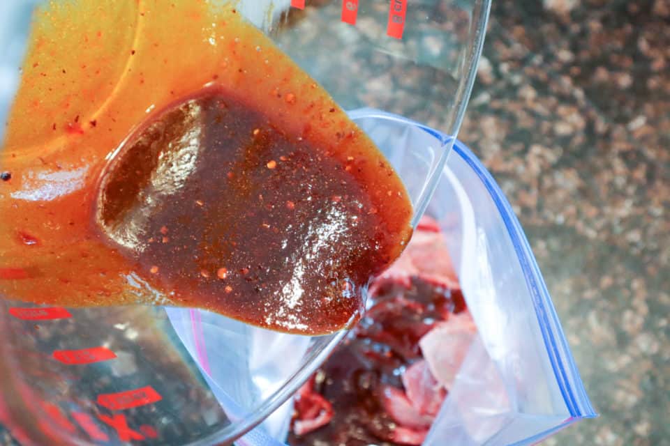 Marinade being poured over the jerky strips in a zip top bag.