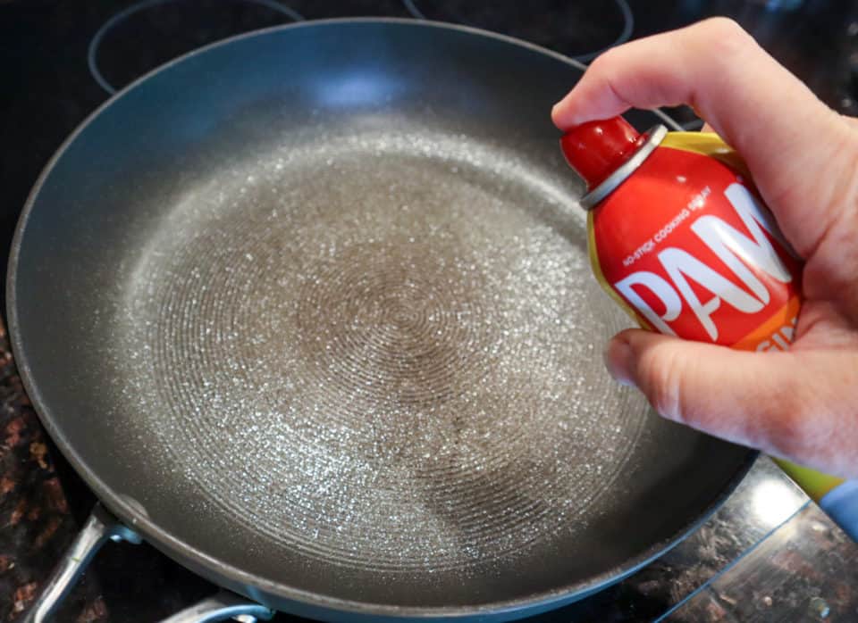 Spraying cooking spray into a skillet.