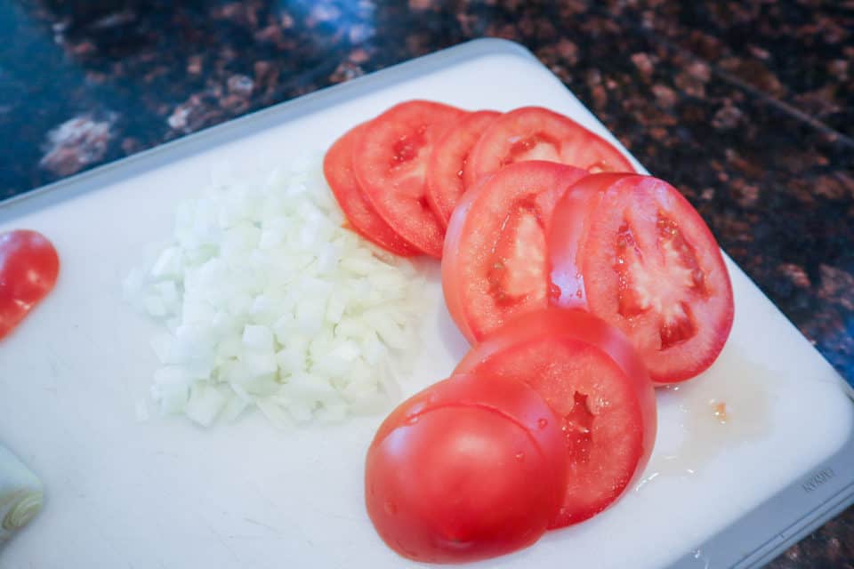 Sliced tomatoes and chopped onions on a cutting board.