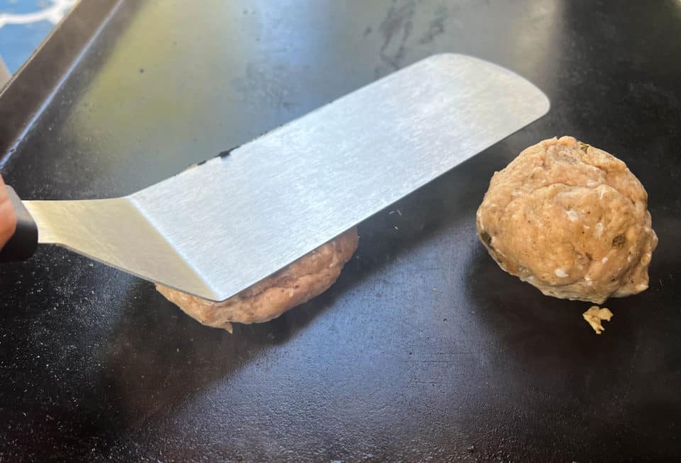 Flattening the Ground Turkey Breakfast Sausage balls into patties with a spatula on the griddle.