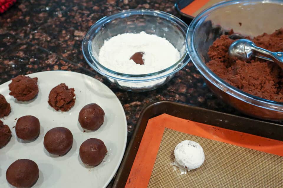 Rolling the dough into balls and then rolling the balls in powdered sugar in a separate bowl.