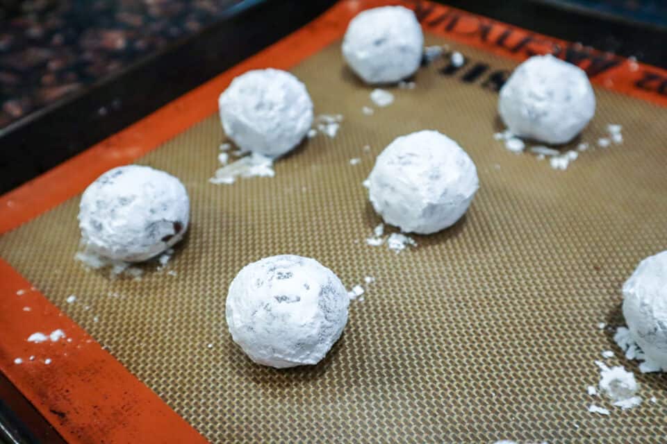 Powdered sugar covered dough balls on a silicone lined baking sheet prior to baking.
