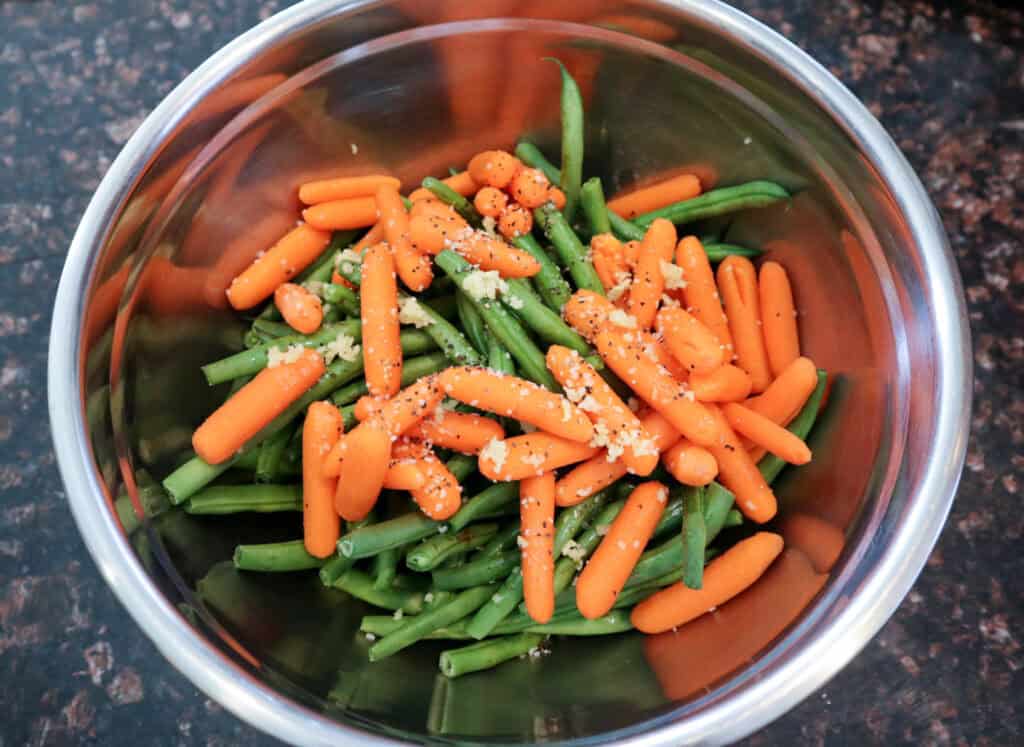 Green beans and carrots with seasonings in a large bowl.