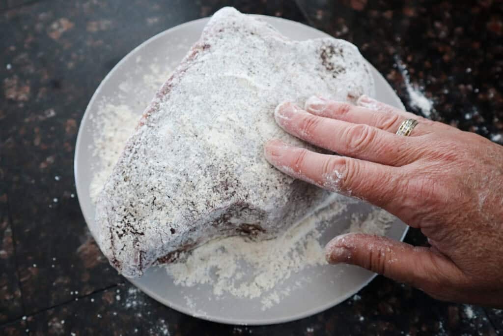 Dredging the beef roast in flour prior to browning.